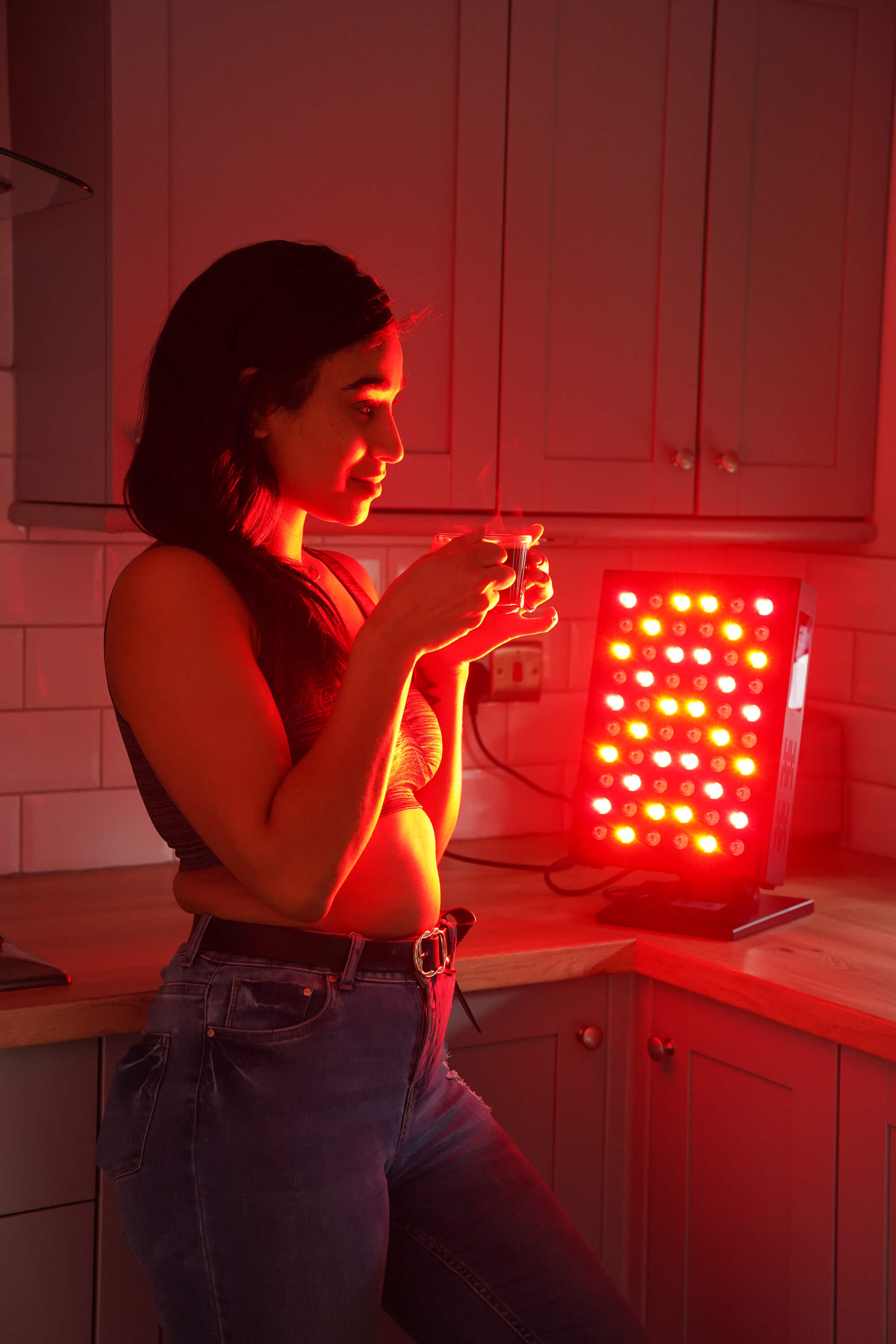 A woman having her cup of tea in front of LumiRed device for better skin health.